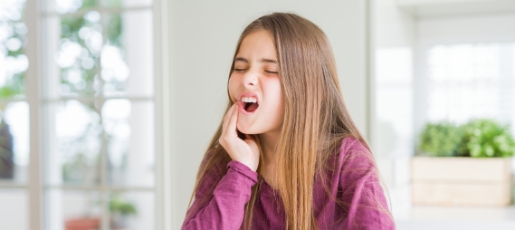 Young girl wincing and touching her cheek