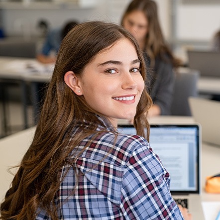 Teen girl smiling while working on computer in classroom