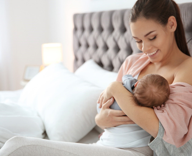 Mother sitting in bed, feeding her baby